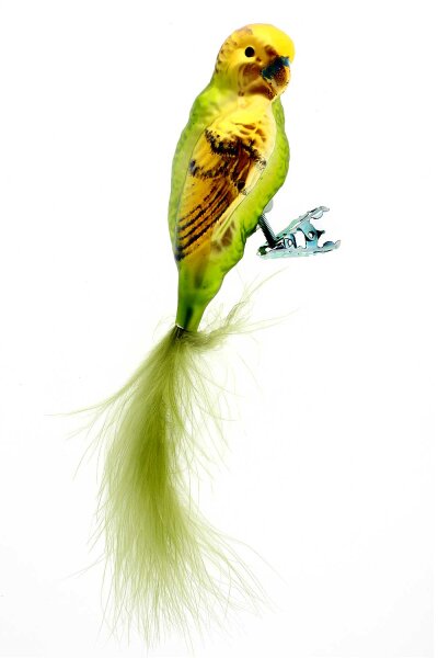 Dieses Bild zeigt eine grüne Glas-Wellensittichfigur, die auf einem Weihnachtsbaum sitzt. Die Figur hat eine leuchtend grüne Farbe und ein glänzendes, reflektierendes Finish.